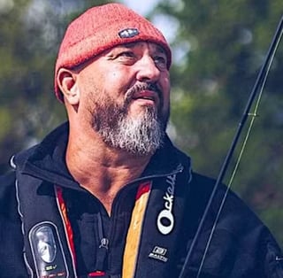 Man med grått skägg och röd mössa som håller i ett fiskespö